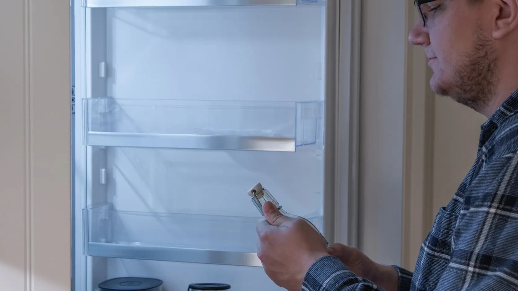 An appliance repair technician inspecting a part in front of an open refrigerator, at work on a service call.