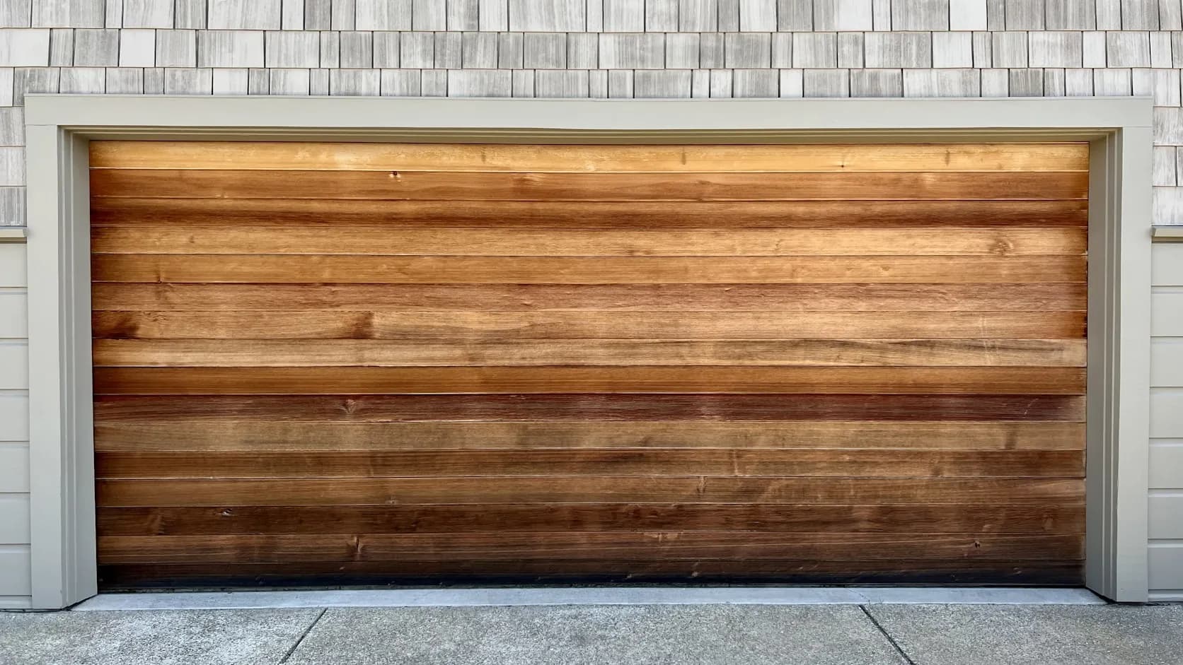 A modern wood-panel residential double garage door, closed, on a clean driveway; best available since Unsplash had no photos of a garage-door tech actively at work.